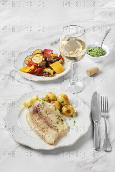 A beautifully arranged dinner includes a plate with a tender fish fillet, roasted potatoes, and colorful vegetables like bell peppers and eggplant