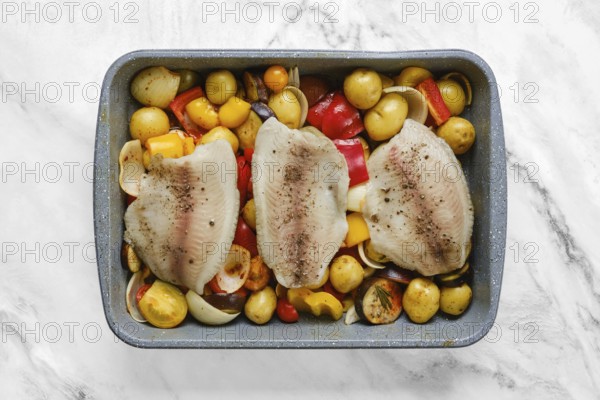 Fish fillets on a bed of colorful roasted vegetables, including onions, peppers, and baby potatoes