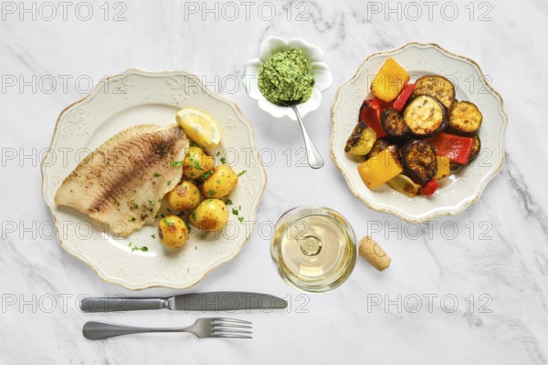 Grilled fish fillet with tender baby potatoes garnished with herbs, alongside a bowl of vibrant roasted vegetables