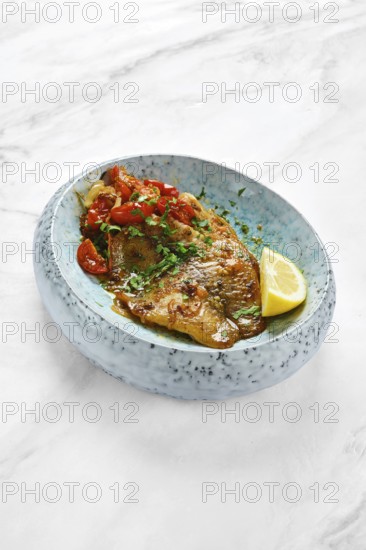 Grilled red seabream fish is topped with fresh cherry tomatoes and herbs, served with a slice of lemon in a modern bowl. This dish embodies a delightful blend of flavors perfect for any meal