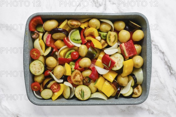 A vibrant mix of fresh vegetables is arranged in a baking tray, showcasing colorful peppers, potatoes, and tomatoes. This healthy preparation is ideal for roasting and enjoying a nutritious dish