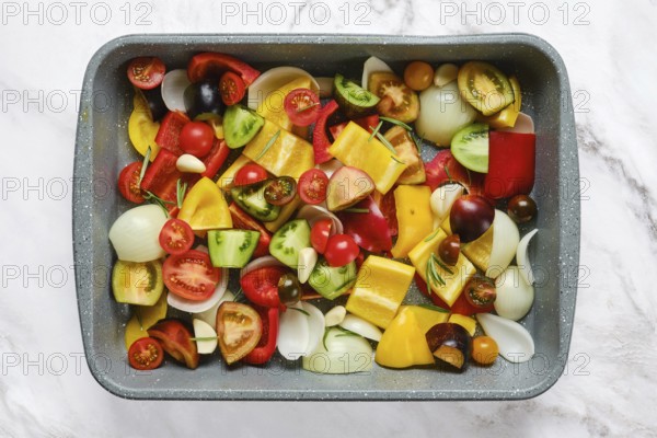 A vibrant mix of fresh vegetables including bell peppers, tomatoes, onions, and zucchini on a baking tray, ready for roasting. The kitchen background suggests a homey atmosphere