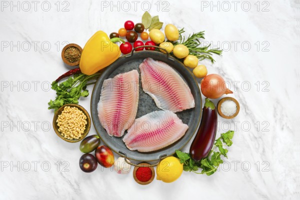 Three raw red seabream fish fillets on a round platter, surrounded by fresh vegetables like peppers, potatoes and tomatoes. Fresh herbs and spices add flavor, making it a perfect setup for cooking
