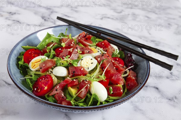 Salad with fresh tuna, cherry tomatoes and quail eggs and avacado, served with chopsticks