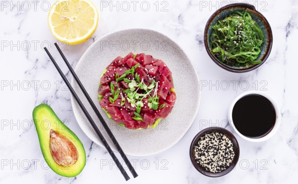 Fresh tuna tartare with avocado served on a marble table with soy sauce and seaweed salad
