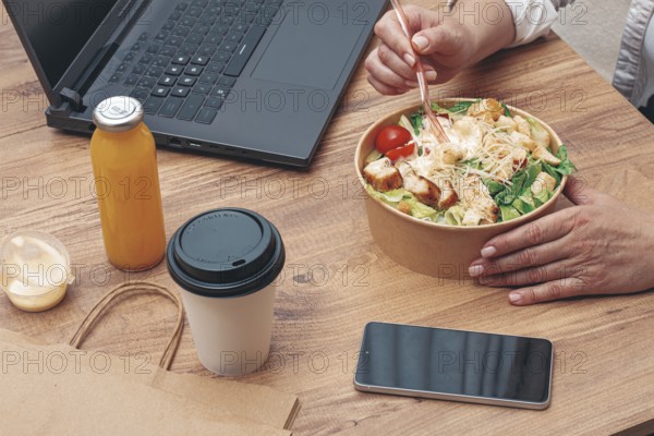 A woman is working on a laptop at home, there is food on the table, salad, coffee and juice, delivery, work at home