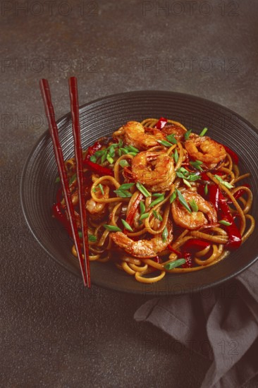 Udon stir-fry shrimp noodles with red bell pepper and green onion, served in a black bowl, with chopsticks, dark background
