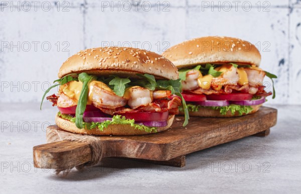 Two shrimp burgers and buns with sesame seeds, bacon, lettuce, tomatoes and onions, On a wooden board
