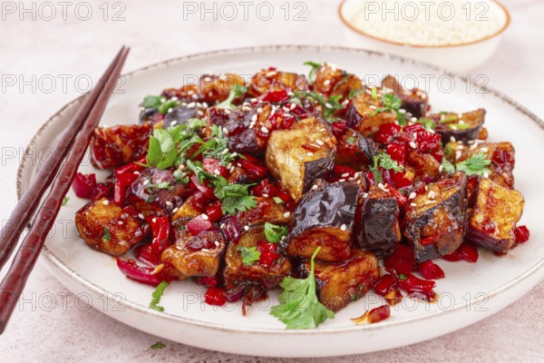 Fried eggplant, Chinese style, in sweet and sour sauce, with pepper and sesame seeds. on a white plate
