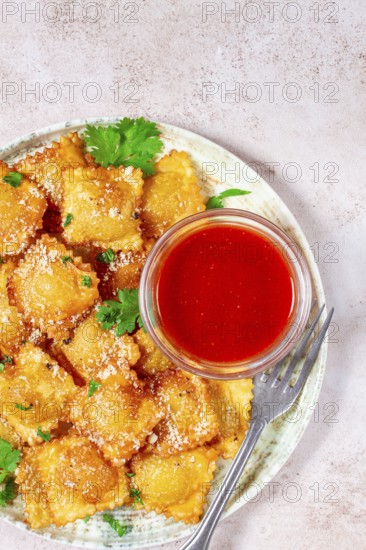 Fried ravioli with parmesan cheese, served with red sauce and garnished with herbs, on a light background, no people