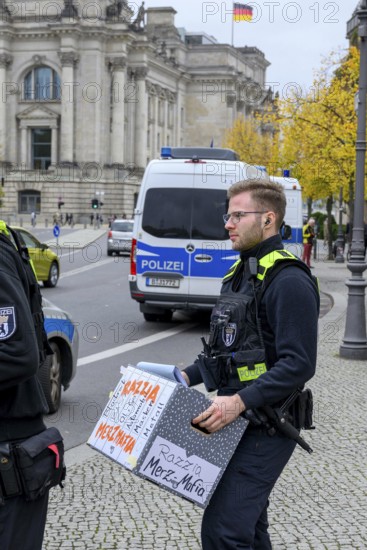 Police officers confiscate boxes from the symbolic house search of the New Generation under the keyword Merz Mafia at the Foundation for Family Business and Politics. The boxes are labelled: Merz Mafia raid, Blackrock, BASF, oil, gas, cars, masks, metal, Bundestag in the background and police cars, Berlin, 10 October 2025