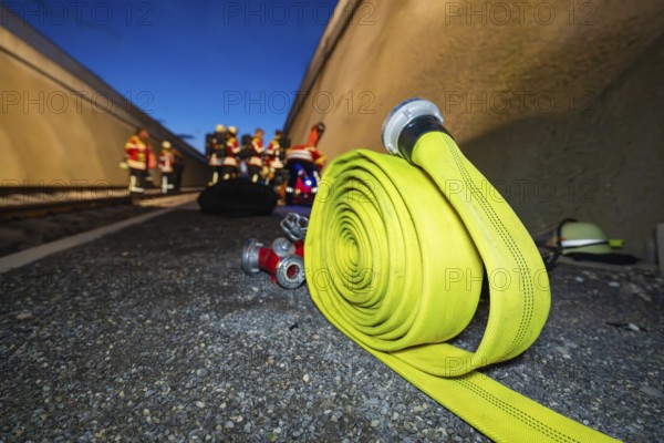 A yellow fire hose lies on the ground, with firefighters in the background, fire drill in the new construction tunnel of the Hermann Hesse railway, Ostelsheim, district of Calw, Germany