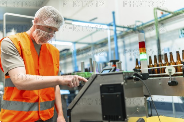 Male worker in protective gear overseeing automated beer bottling and labeling on a clean modern conveyor line, monitoring machinery for quality control and safe production standards