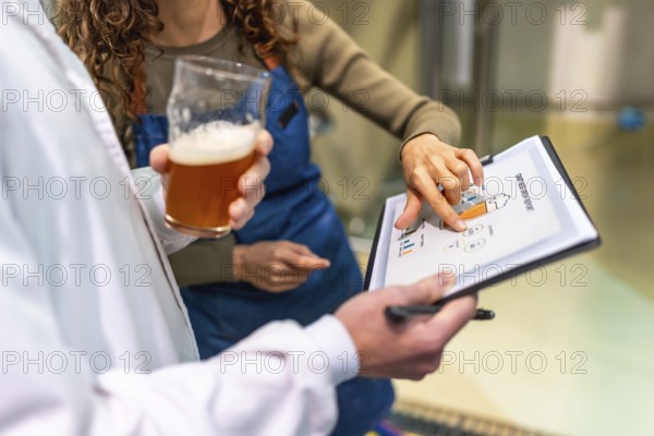 Brewery staff discussing quality control data and production metrics from a clipboard report while holding a fresh glass of craft beer, ensuring optimal brewing conditions and product standards