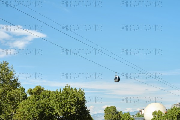 A cable car travels smoothly across a bright sky, suspended over a rich canopy of trees