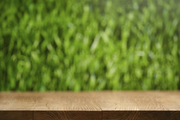 A simple wooden table stands in front of a softly blurred lush green grass background. The scene captures a sense of nature and tranquility. Ideal for outdoor dining or relaxation moments