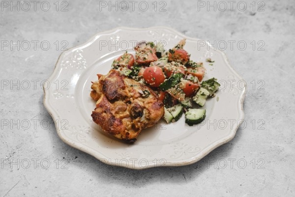 A hearty baked dish sits on a decorative plate alongside a vibrant vegetable salad. The salad features fresh tomatoes and cucumbers, creating a colorful and nutritious meal perfect for any time