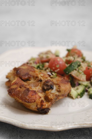 Juicy chicken piece rests on a plate beside a colorful salad made of tomatoes, cucumbers, and herbs. This meal showcases fresh ingredients perfect for a healthy lunch or dinner