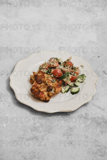 A delightful meal features a colorful salad with tomatoes and cucumbers placed beside a savory baked dish. The food is arranged on a decorative plate on a neutral background