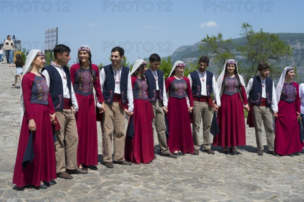 Group in red traditional costumes dancing together on cobblestones against a mountain backdrop, folklore, Tatev, Tatev, Syunik province, Syunik, Armenia
