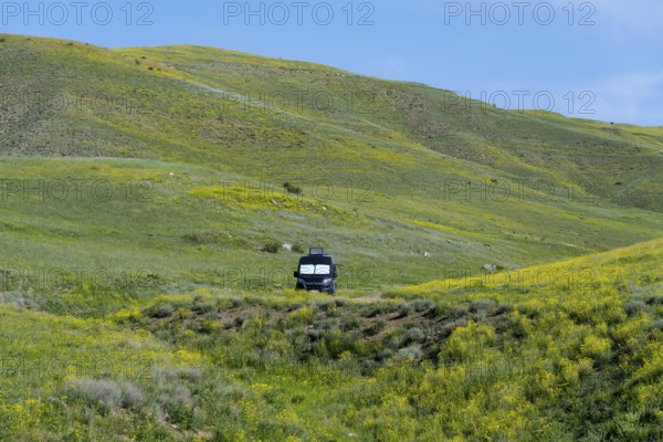 A black van stands alone in a meadow next to green and yellow hills under a blue sky, camper, landscape near Hatsavan, Kotayk province, Kotayk, Armenia