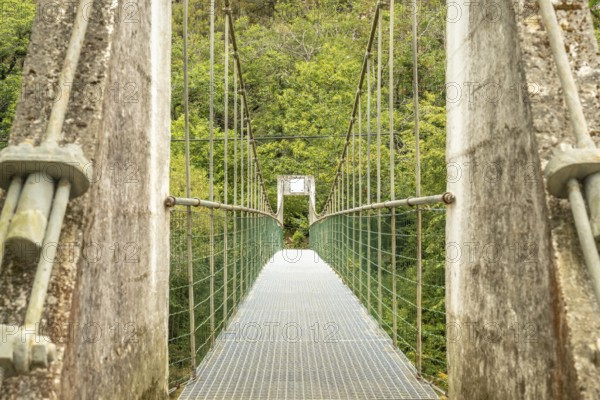 Metal suspension bridge crossing the sella river, connecting the dobra river route with the olla de san vicente, surrounded by lush vegetation in asturias, spain