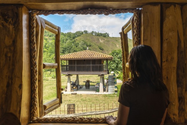 Tourist enjoying the serene view of a traditional asturian horreo from a cozy wooden cabin in the charming village of benia de onis, asturias, spain