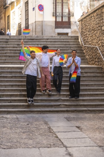 Young friends are celebrating lgbtq plus pride by walking down urban stairs, holding a large rainbow flag, a small flag, and a fan, expressing joy and unity