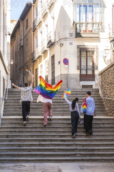 Young adults are joyfully walking up stone stairs in a european city, carrying rainbow flags and a bag, celebrating diversity and the lgbtq plus community during a pride event