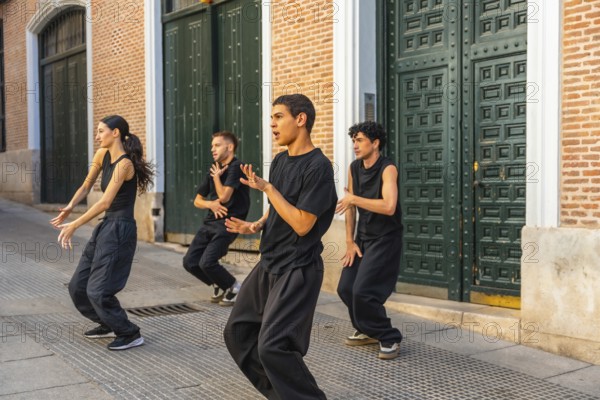 Group of young contemporary dancers moving in sync, expressing their art during a street performance in an urban setting with a historical brick building and large green door