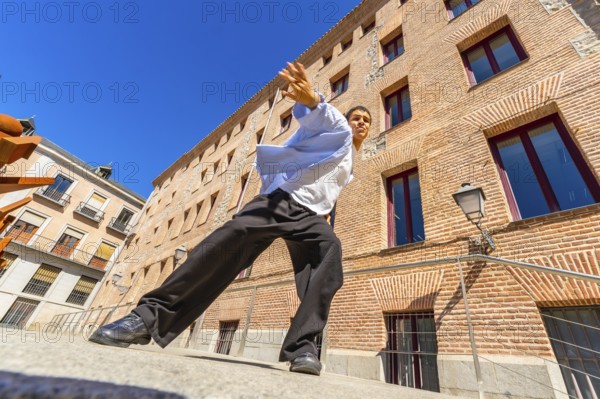 Young man actively performing a passionate flamenco move on a city street, expressing cultural artistic movement against a traditional brick building under a clear blue sky