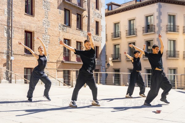 Group of diverse urban dancers performing synchronized street dance movements with raised arms and dynamic poses on a sunny city square, expressing energy and freedom through their art