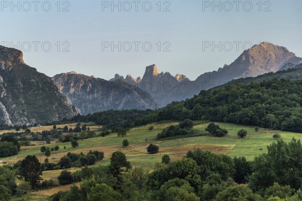 Golden hour sunlight illuminating the iconic naranjo de bulnes peak, towering over lush green valleys and forests in picos de europa national park, asturias, spain