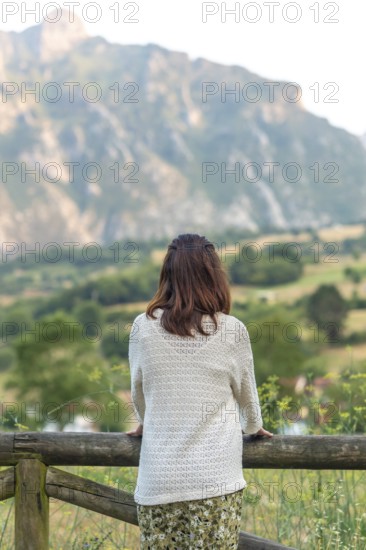 Woman leaning on a wooden fence, admiring the breathtaking view of picu urriellu, a stunning peak in picos de europa national park, asturias, spain