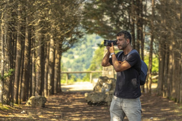 Male photographer taking pictures with professional camera in a forest near a viewpoint in benia de onis, asturias, spain, during a sunny summer day