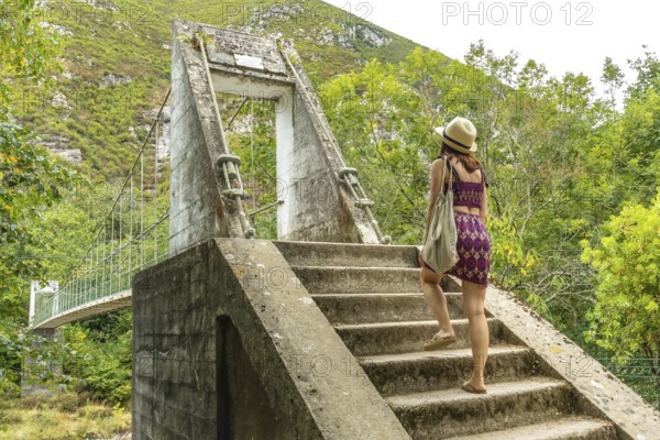Female tourist walking up concrete stairs leading to an old suspension bridge over the dobra river in asturias, spain, enjoying the beautiful natural scenery and embarking on an adventurous journey