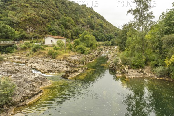 Sella river meandering through a rocky riverbed, surrounded by lush vegetation, trees, and a small white house on the riverbank, creating a picturesque scene in asturias, spain