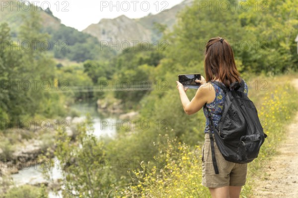 Female tourist with a backpack capturing photos of the dobra river along the scenic route to olla de san vicente in asturias, spain, on a sunny summer day