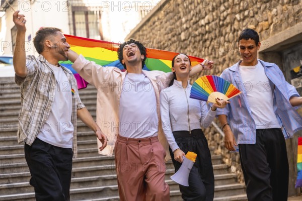 Group of young friends celebrating equality and diversity, walking happily in a city street during a pride parade, waving a rainbow flag and carrying a megaphone and a fan