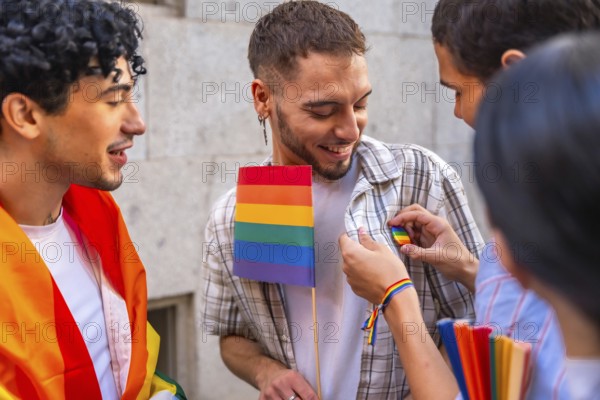 Group of young people smiling and interacting at a pride event, one person receiving a rainbow pin while holding a small rainbow flag, symbolizing pride, acceptance, and community