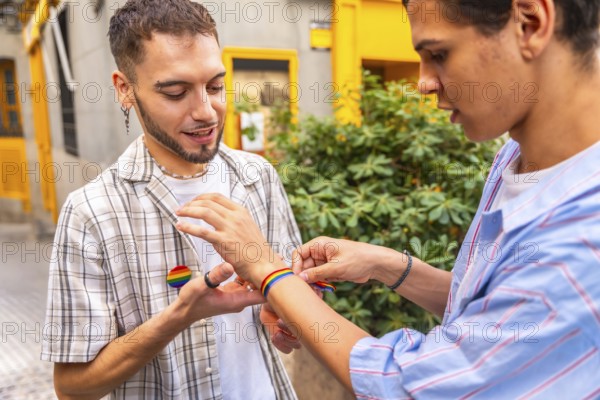 Two men clasp hands and put on rainbow flag bracelets outdoors, celebrating love, pride and identity with affectionate, candid street style connection and joyful solidarity