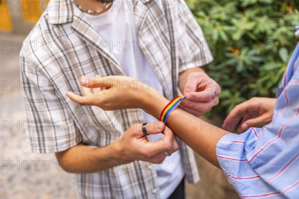 Two hands fastening a colorful rainbow bracelet on a wrist outdoors, symbolizing pride, love and solidarity in the lgbtqia plus community at a parade or festival celebration