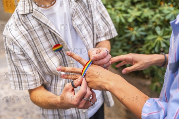 People are decorating their hands with rainbow colored adhesive tape, celebrating identity, community, and pride, with a rainbow pin visible on one person's shirt