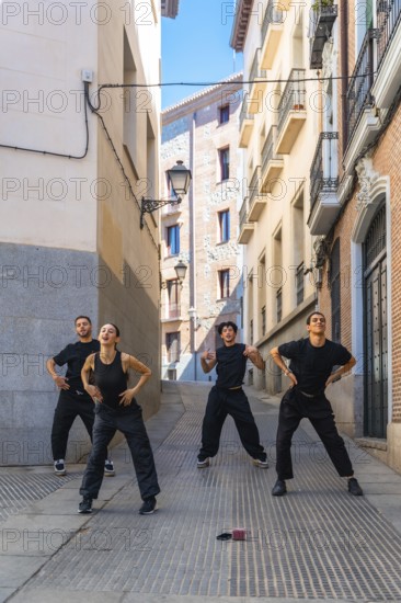 Group of diverse young adults expressing themselves through dynamic street dance movements on a paved urban alleyway, confidently performing in uniform black clothing during daylight