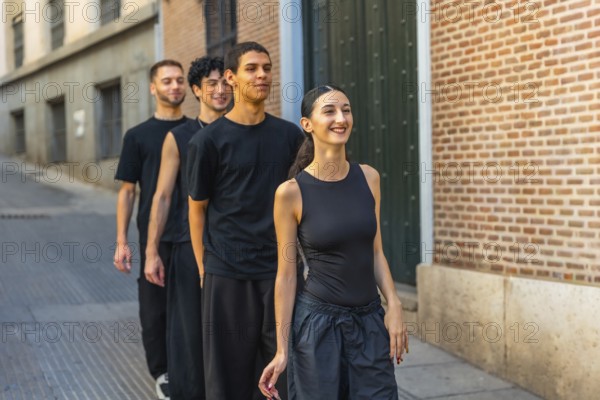 Young diverse dancers walking in line down a city street, smiling and energized while rehearsing choreography outdoors against brick buildings, joyful teamwork and movement
