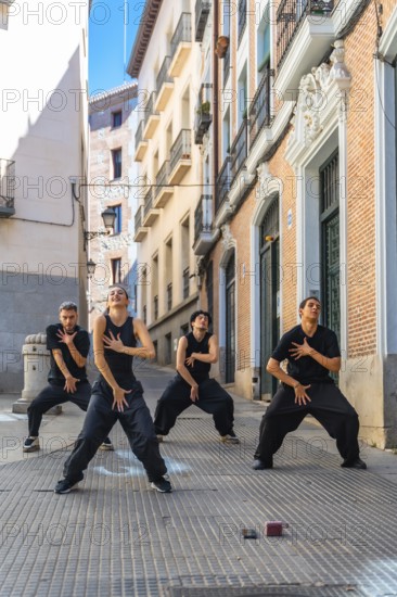 Group of four young dancers expressing movement and energy through a choreographed street performance in a narrow european alley, showcasing contemporary dance