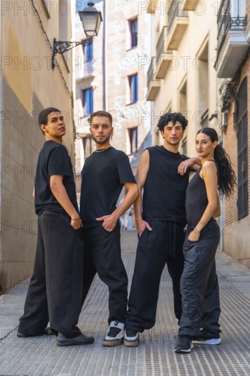 Four young adults in coordinated black streetwear pose confidently on a cobblestone alley, full length group portrait blending urban fashion, dance attitude and close knit friendship