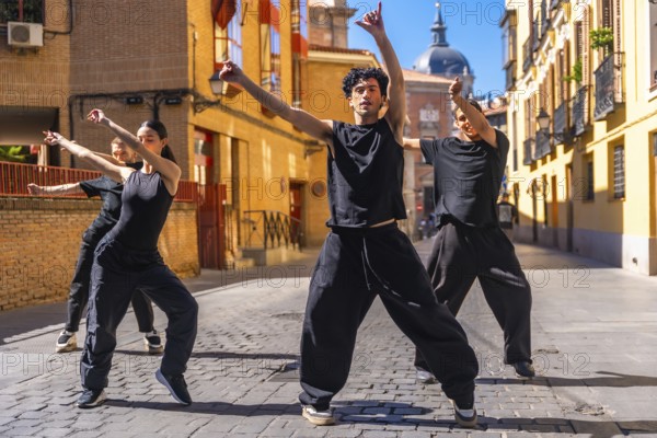Group of four youth street dancers dressed in black performing contemporary choreography in a compact urban setting on a sunny day, showcasing artistic freedom and urban culture