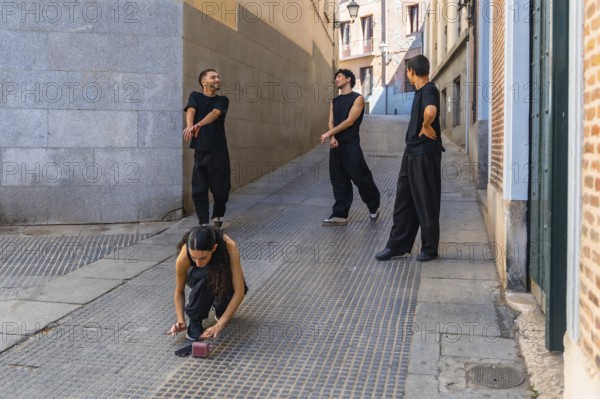 Group of young friends wearing black clothing rehearsing a contemporary dance routine on a cobblestone street in an old city alley, practicing their moves and enjoying the creative process outdoors