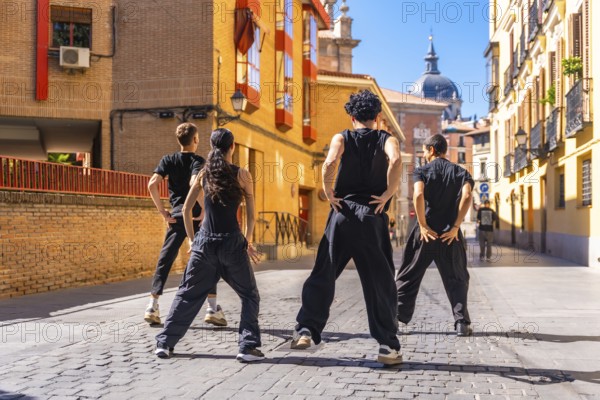 Group of young people standing in an urban cobblestone street, performing an energetic street dance routine together, showcasing teamwork and youthful expression